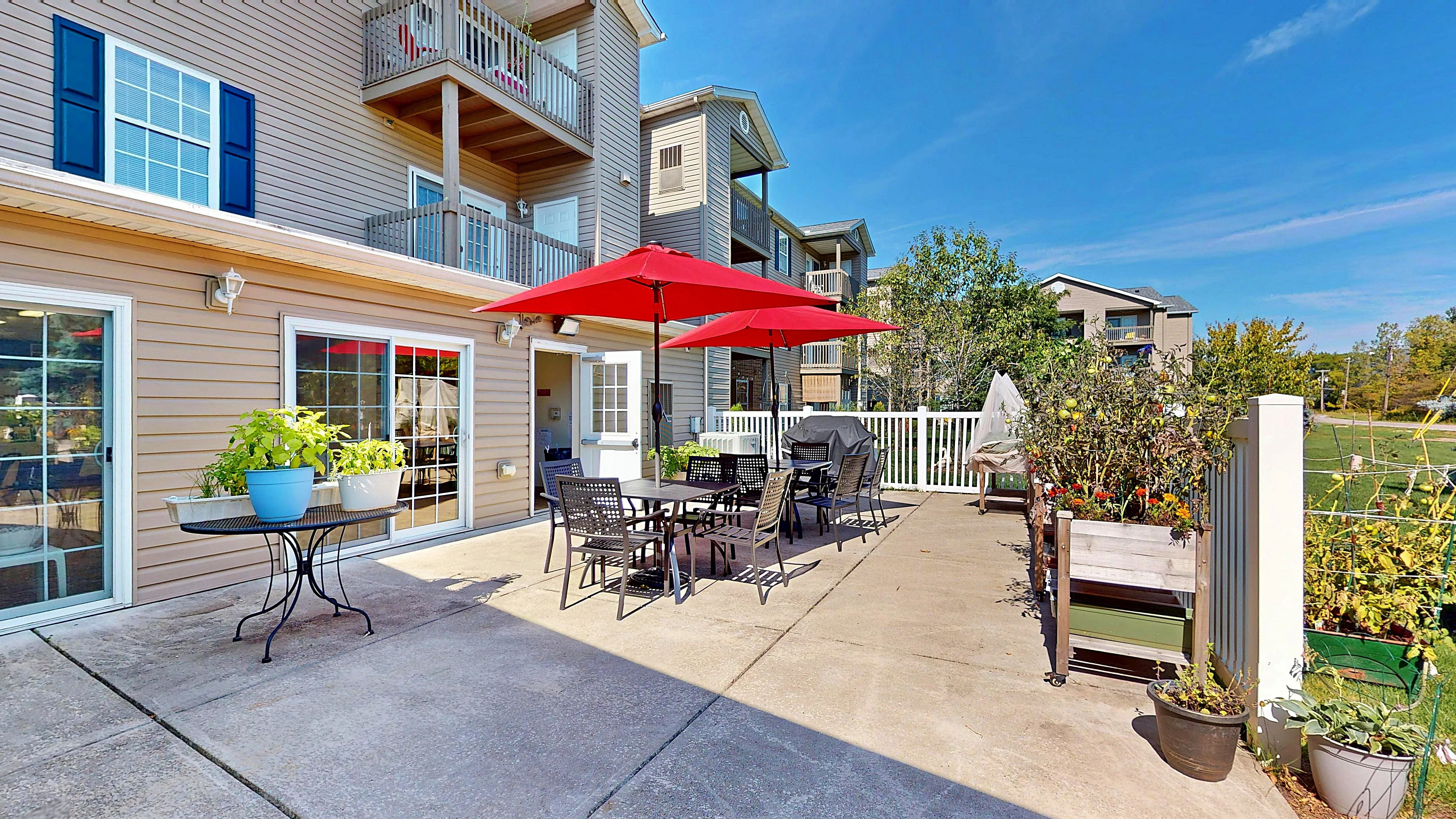 Charming apartment patio with vibrant red umbrellas, potted plants, and ample seating for outdoor relaxation, set against a backdrop of modern architecture.