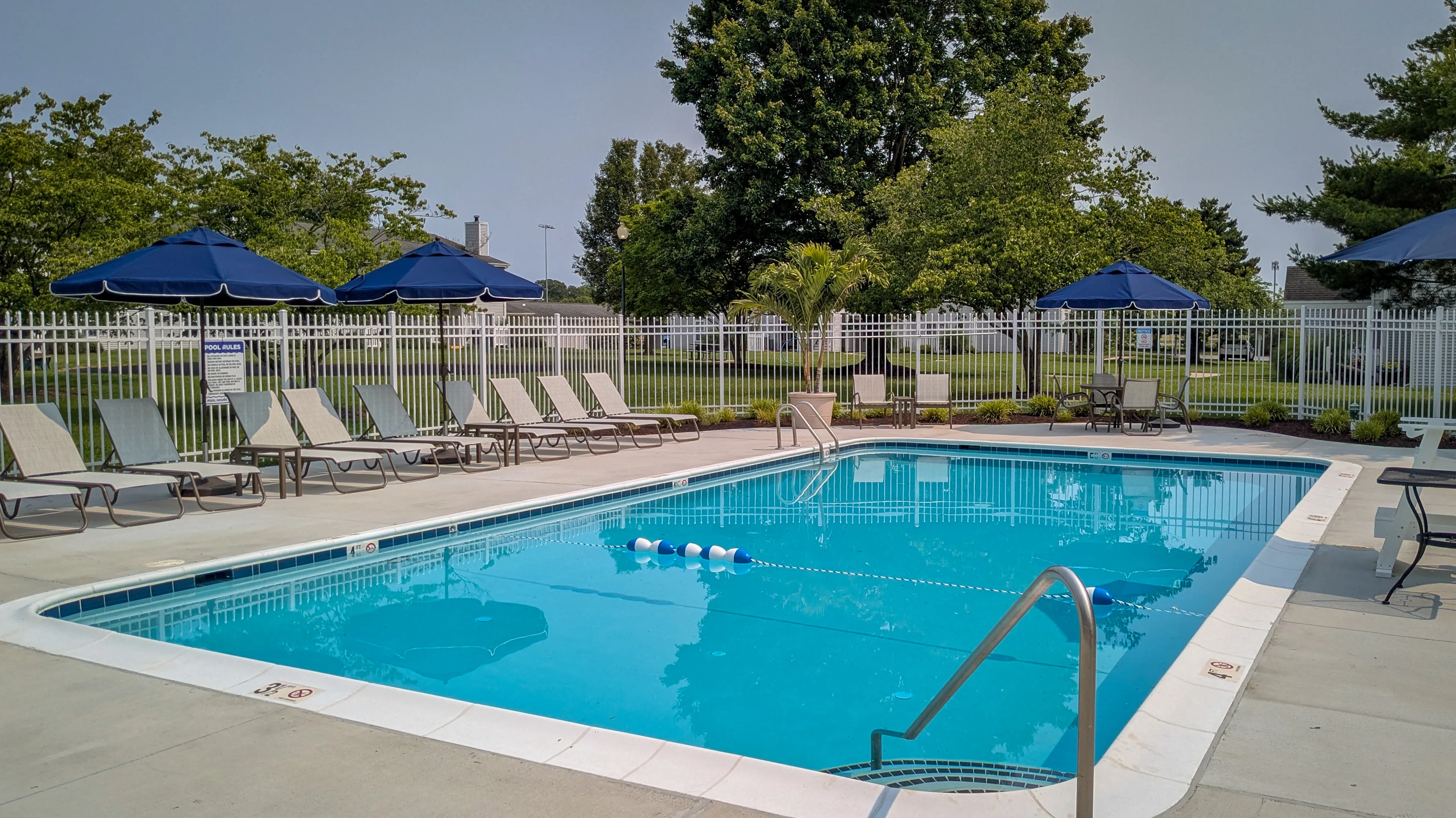 Inviting outdoor pool area with blue umbrellas, comfortable loungers, and lush greenery, perfect for relaxation and leisure.