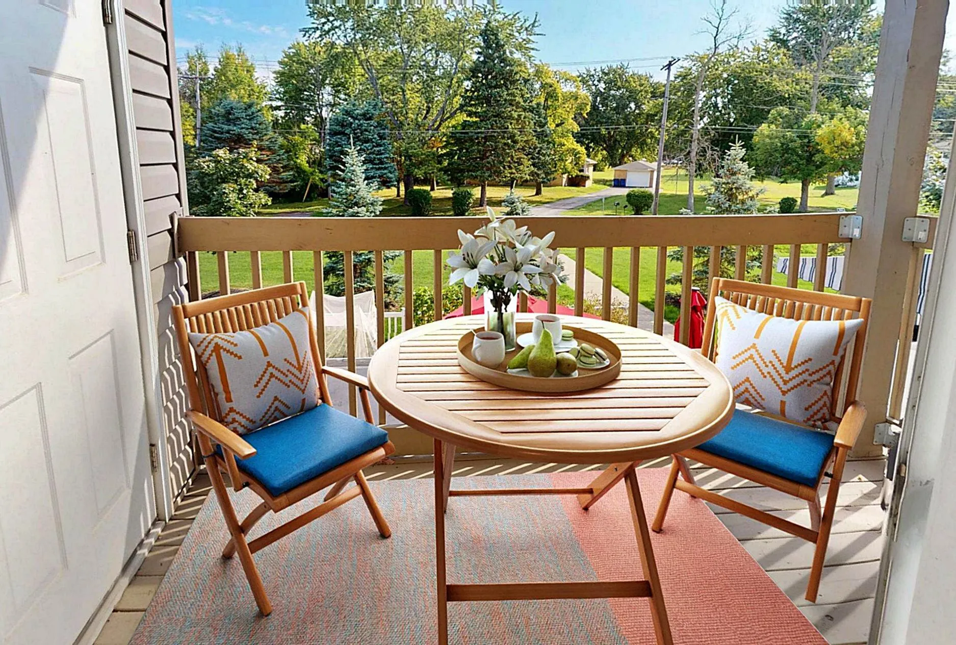 Charming balcony with cozy wooden chairs and a round table, offering a lush green view, perfect for relaxation.