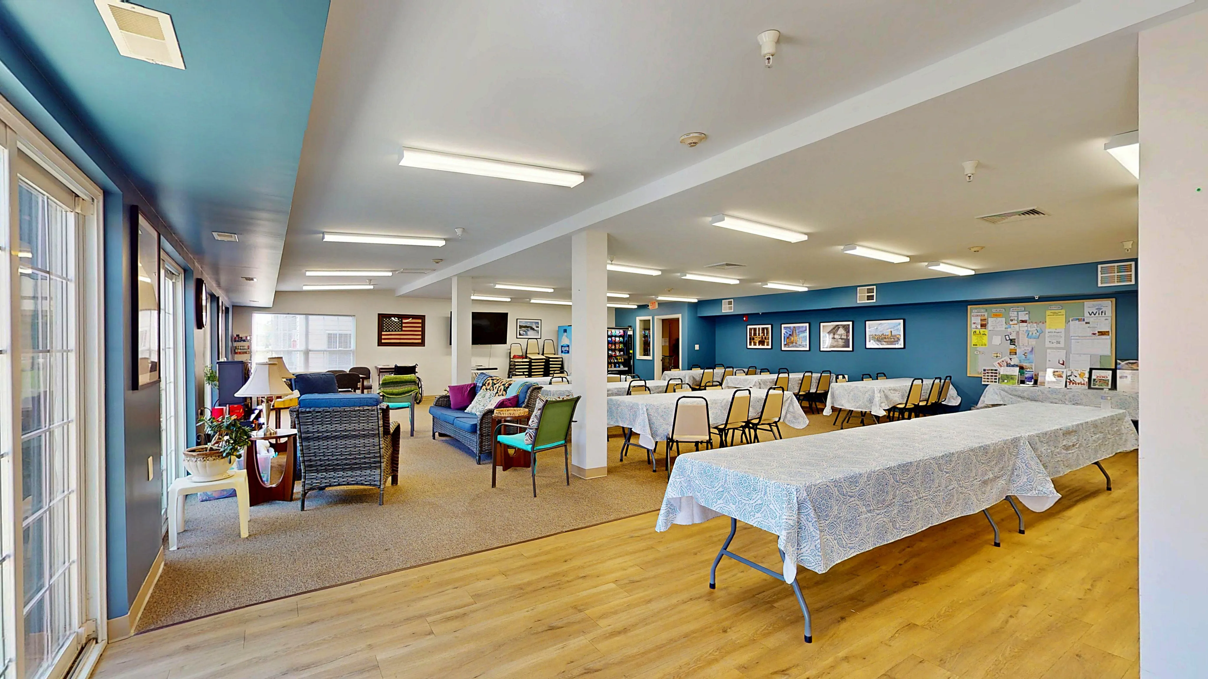 Vibrant community room featuring stylish seating areas, a wall of windows, and ample dining space framed by elegant blue accents.