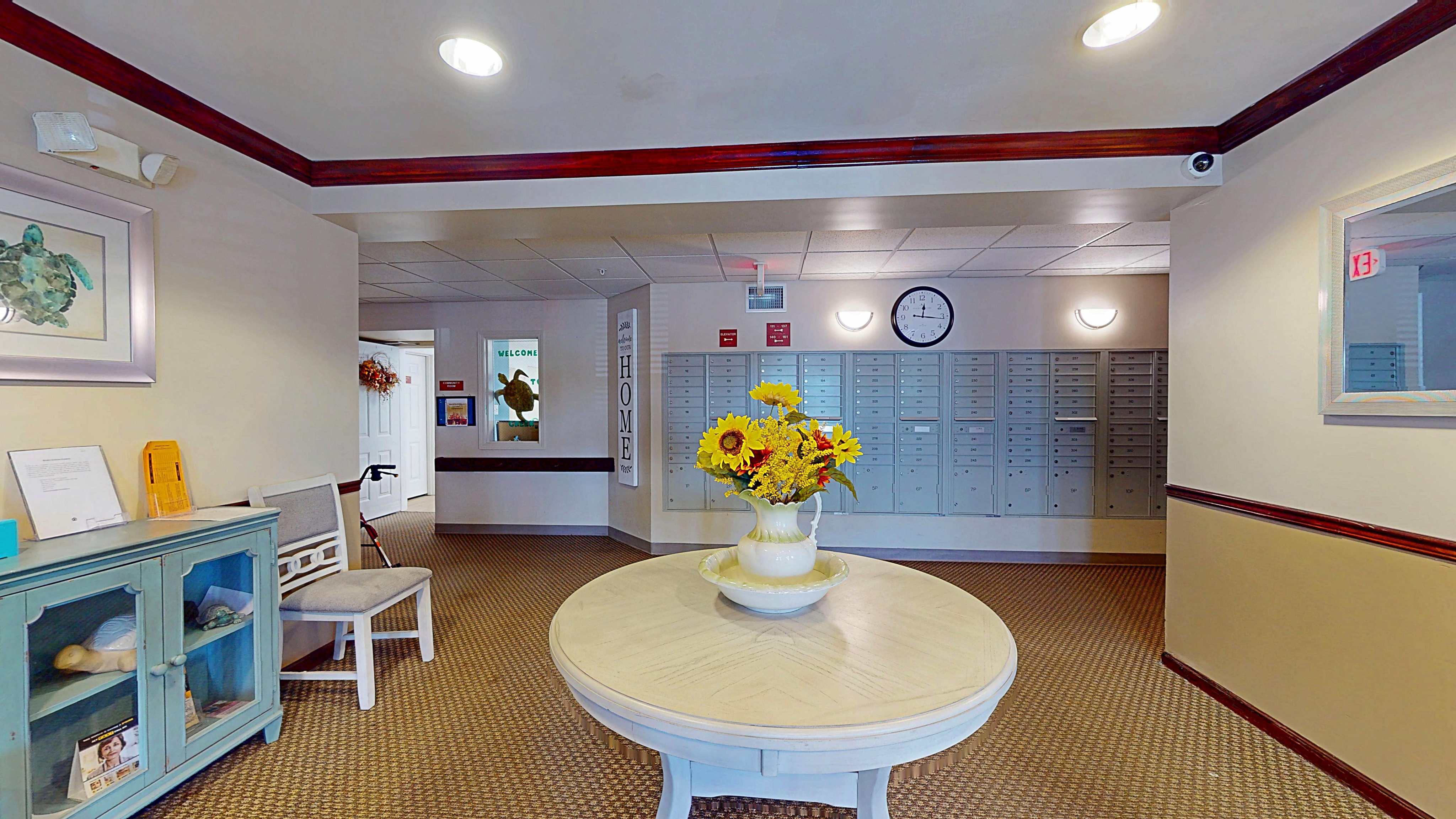 Charming apartment lobby featuring a round table with vibrant sunflowers, vintage-style mailboxes, and elegant decor, creating a welcoming ambiance.