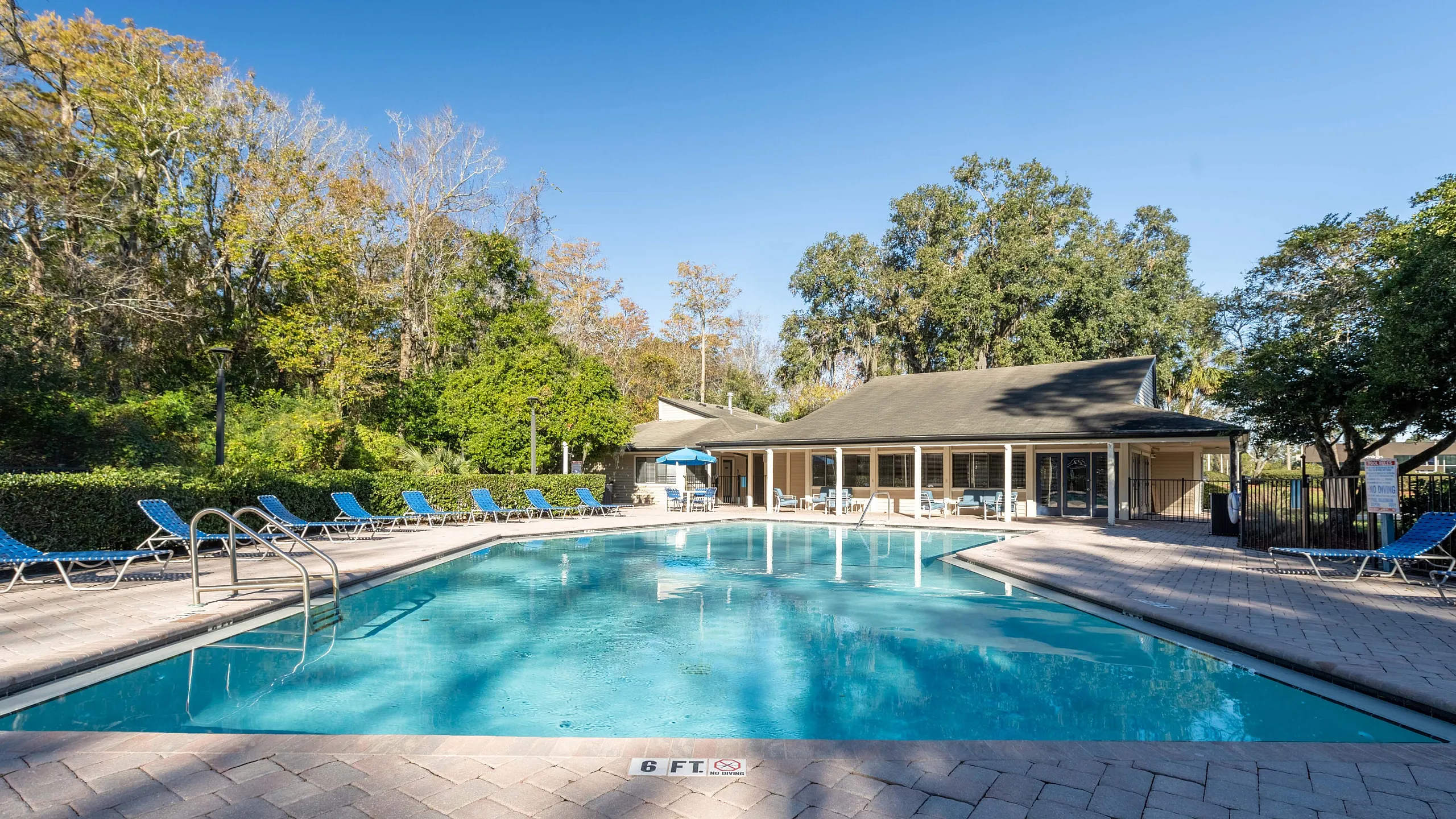 Inviting outdoor pool with surrounding lounge chairs and lush greenery under a clear blue sky.