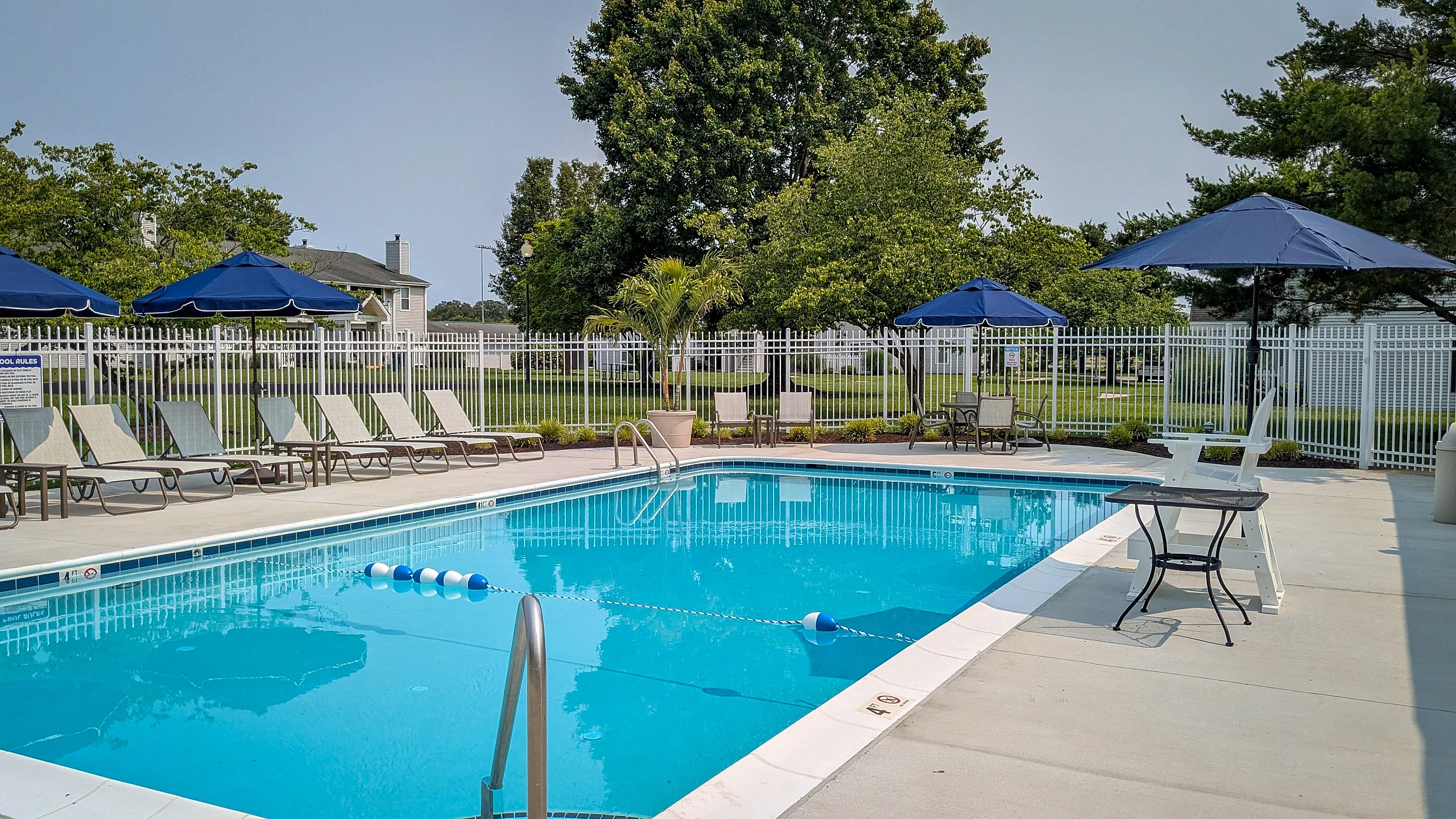 Inviting outdoor pool with elegant lounge chairs and large blue umbrellas, set against a backdrop of lush greenery, perfect for relaxation.