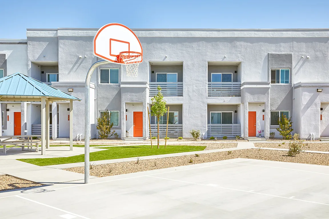 Contemporary apartment complex featuring vibrant orange doors, balconies, and a basketball court in the foreground.