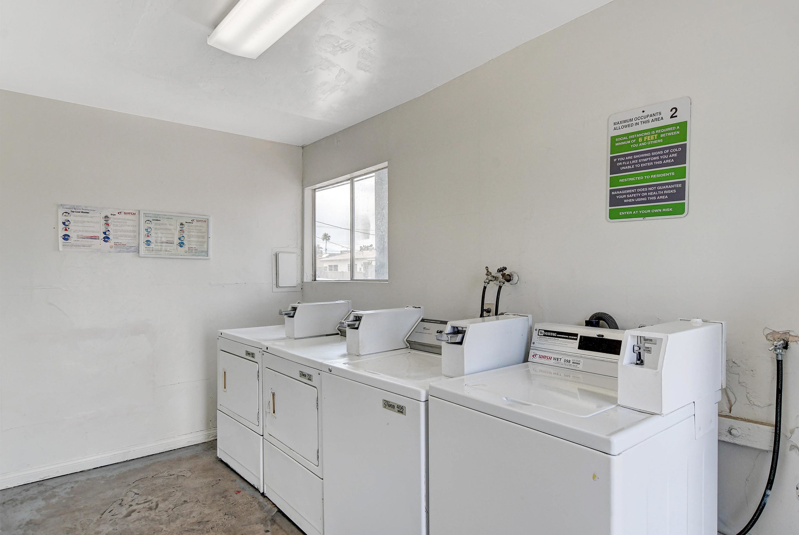 Well-lit laundry room featuring white washing machines and dryers with clear signage on the wall.