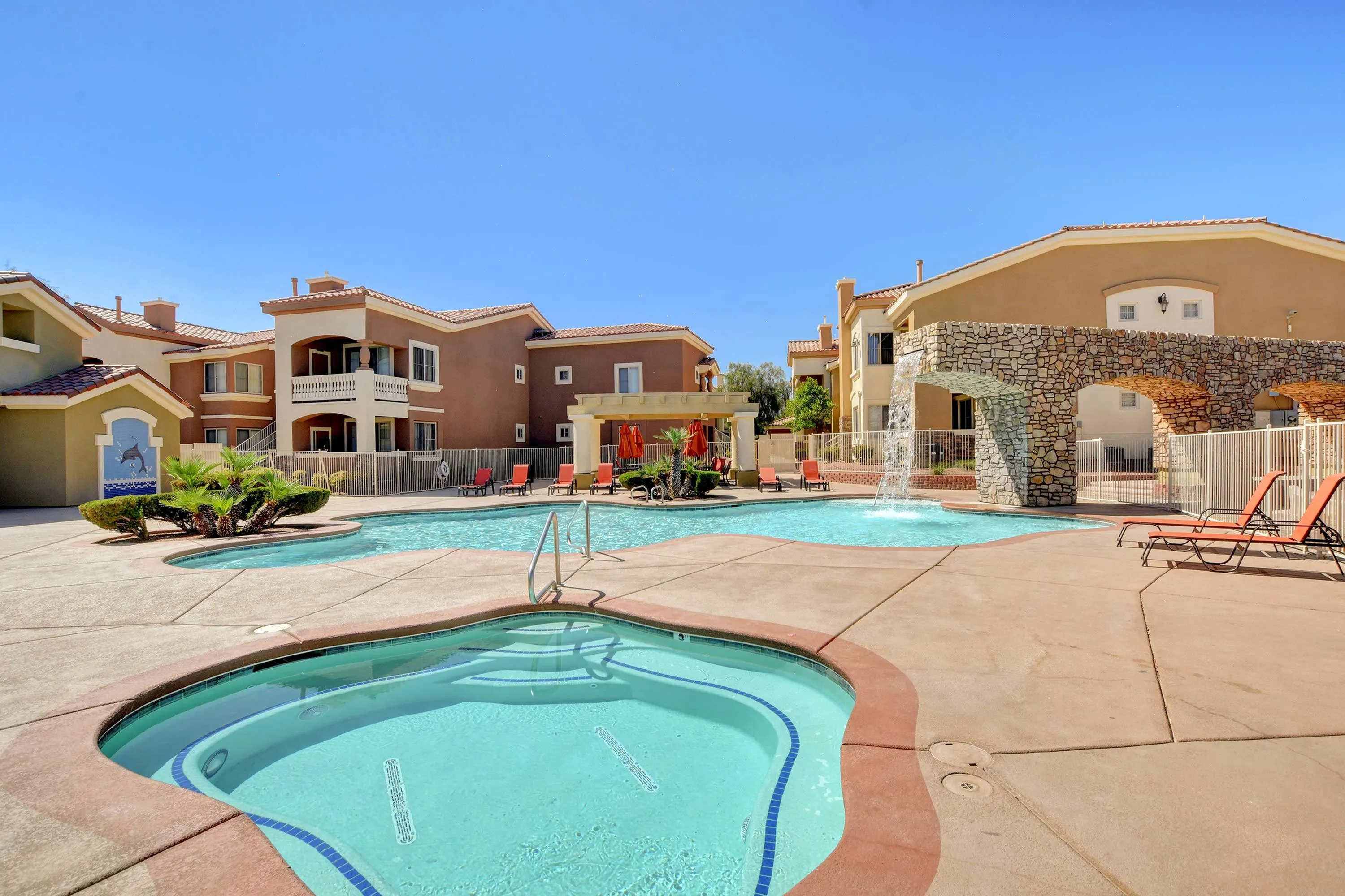 Elegant apartment complex featuring a stunning pool with a waterfall and cozy outdoor seating.
