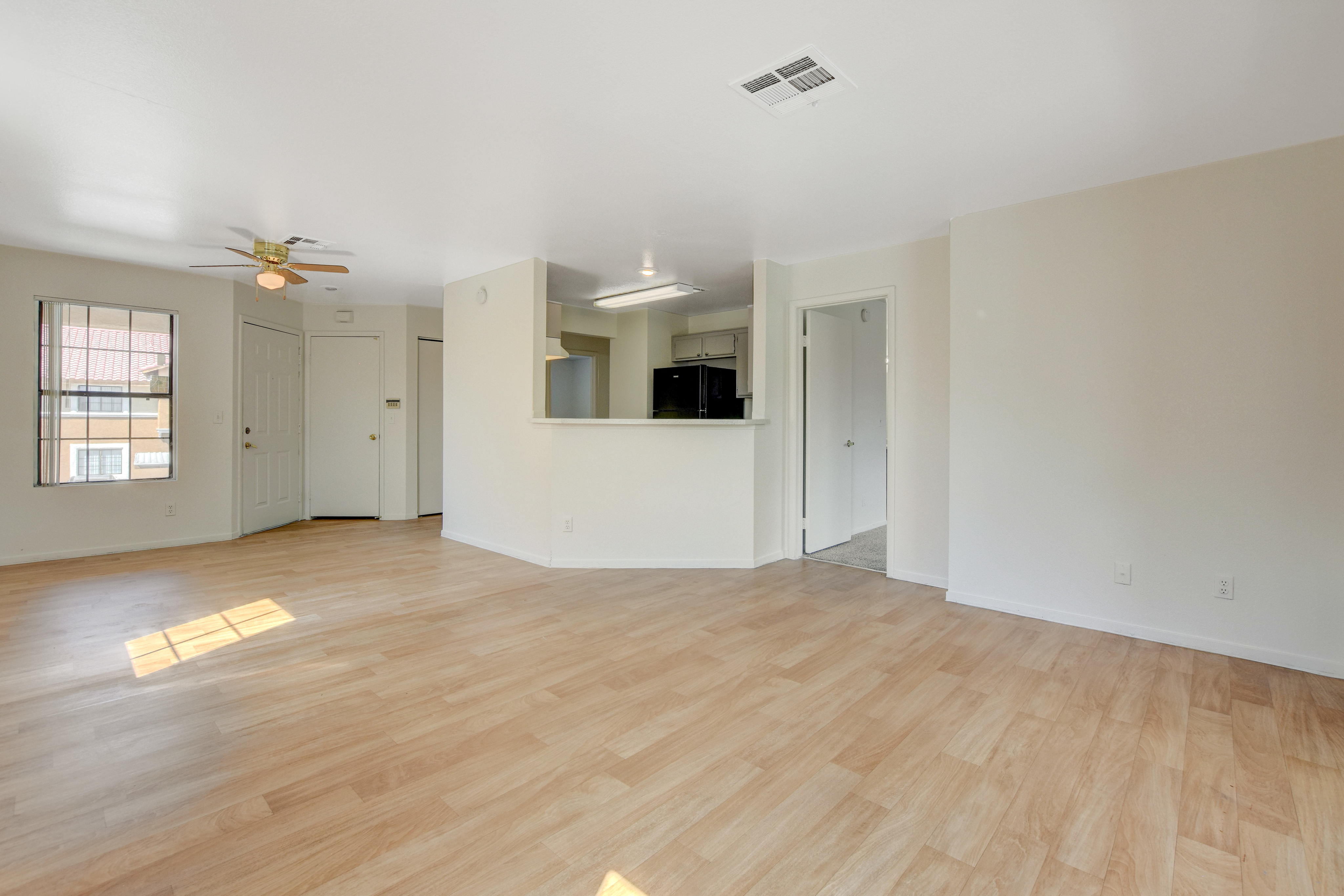 Bright and airy living room with laminate flooring, a ceiling fan, and access to the kitchen.