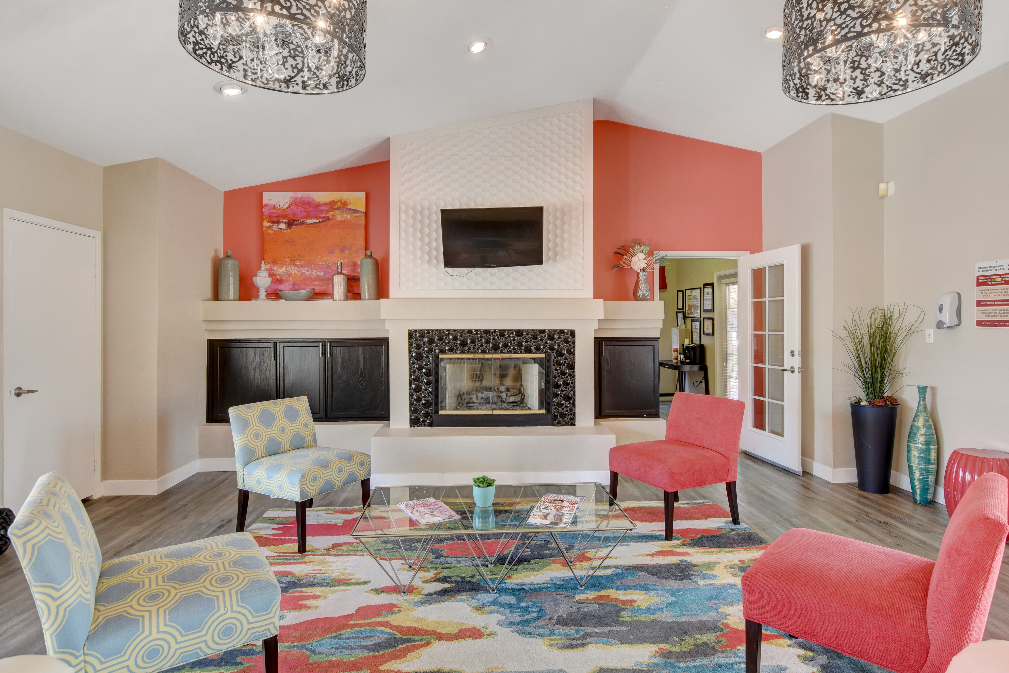Stylish modern living room with vibrant decor, featuring colorful chairs, a decorative fireplace, and a contemporary chandelier.