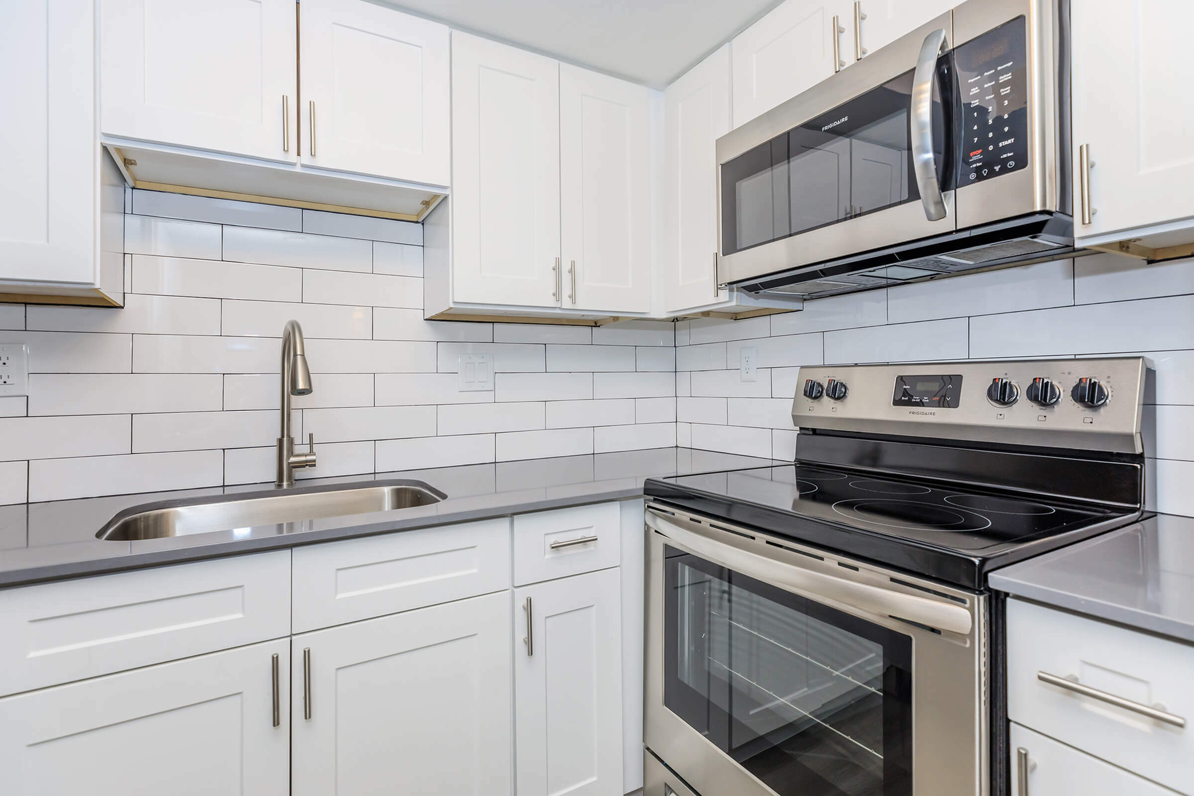 Contemporary kitchen featuring white cabinets, stainless steel appliances, and a sleek grey countertop.