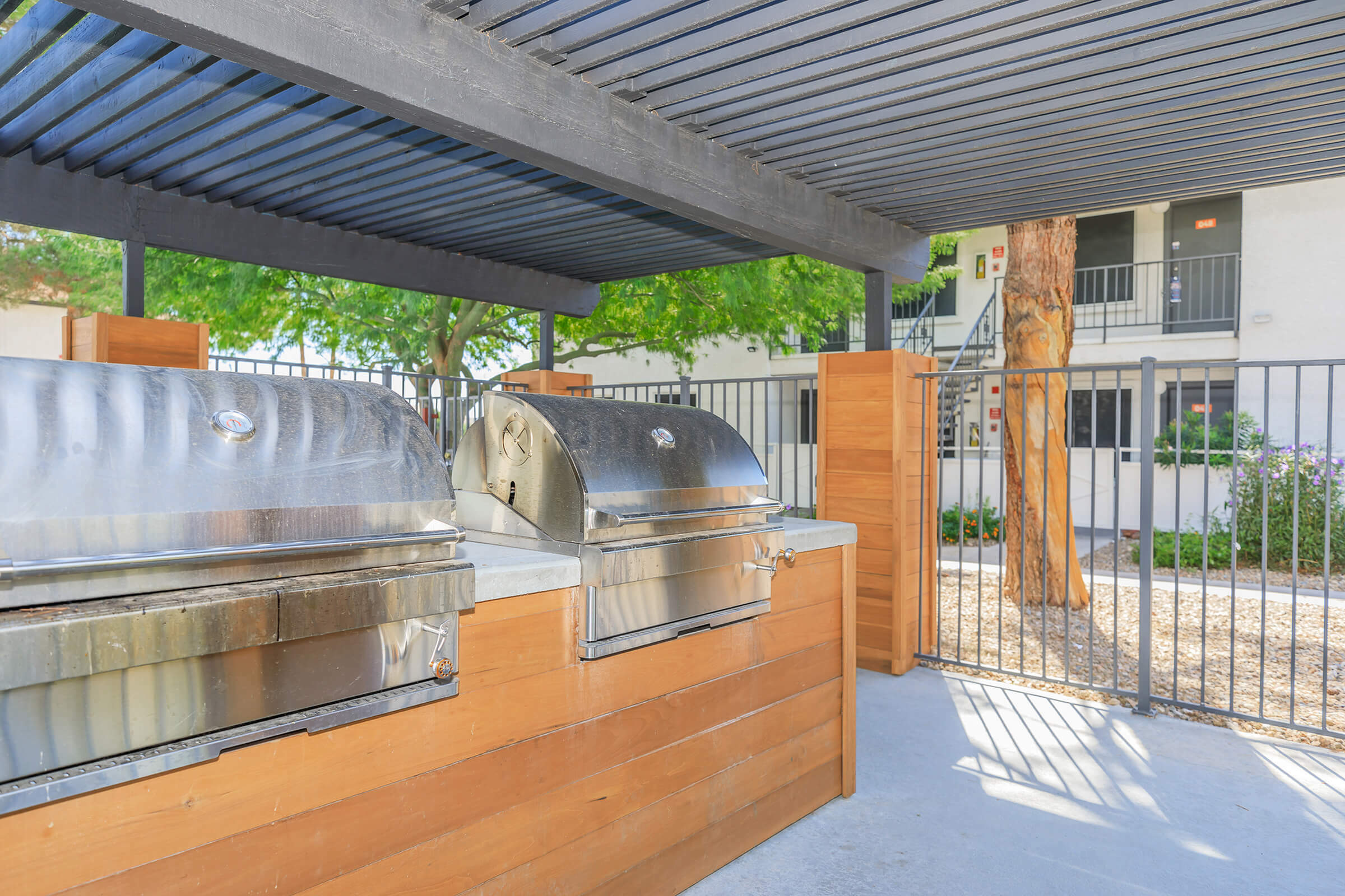 Elegant outdoor BBQ space with stainless steel grills and a stylish wooden countertop under a sleek pergola.