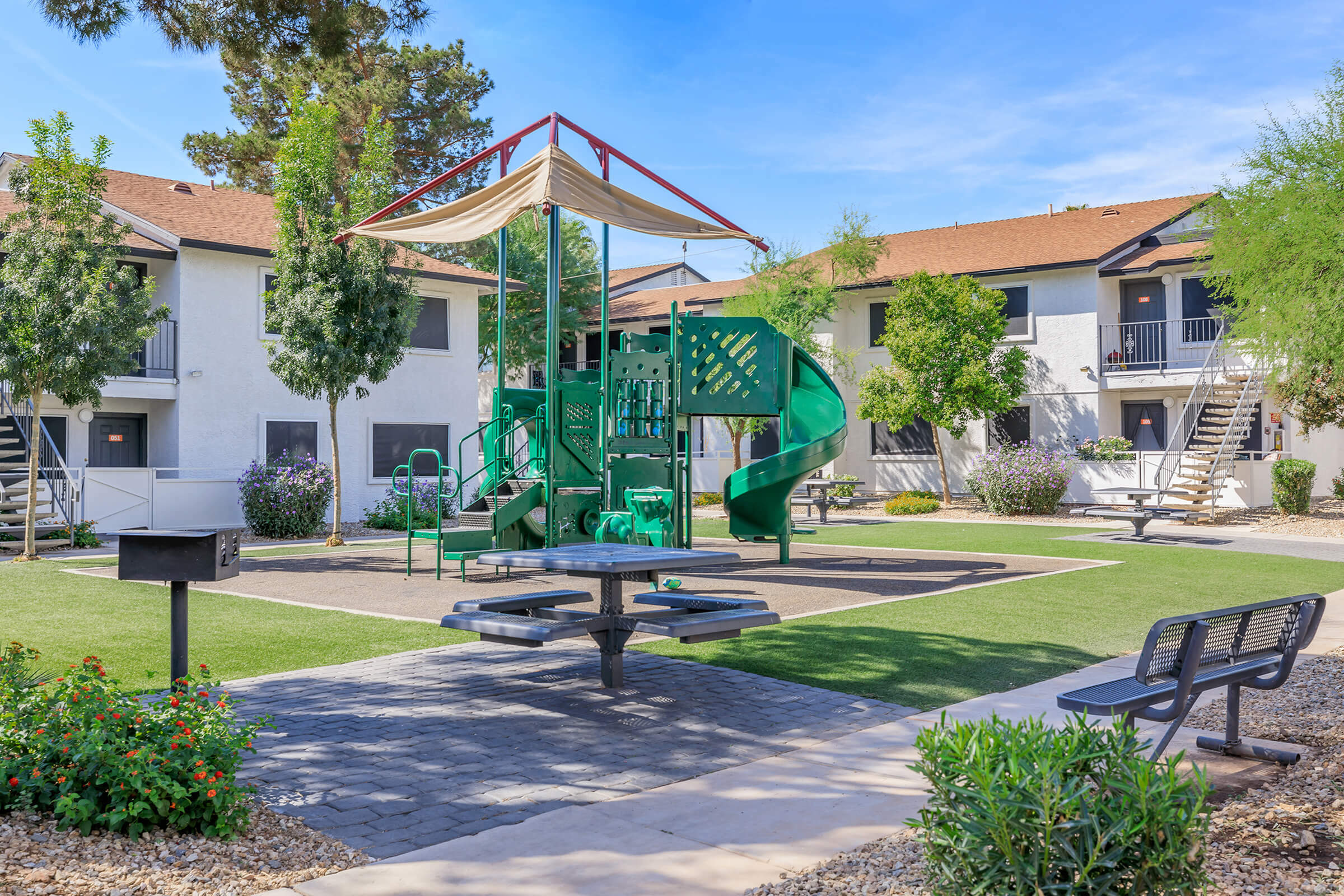 Inviting apartment complex courtyard featuring a modern playground with slides, lush greenery, and comfortable seating areas.