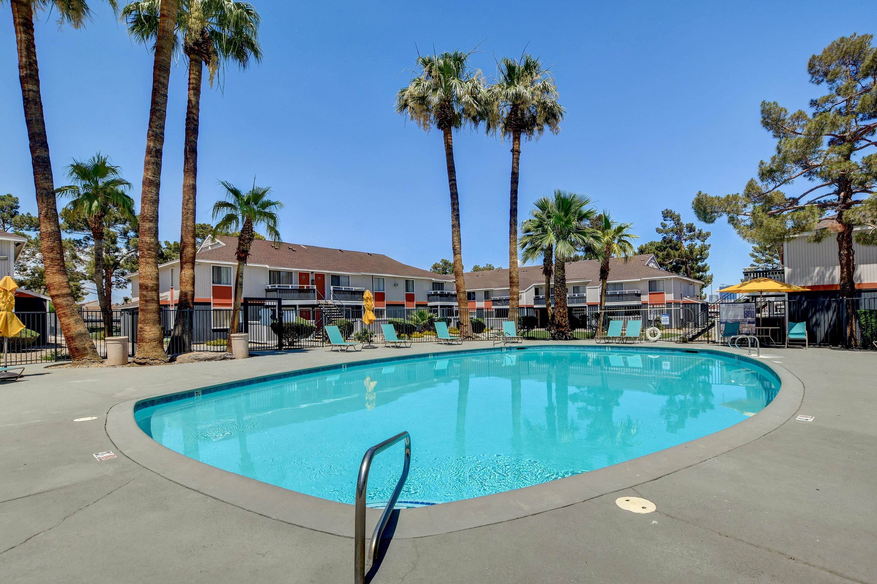 Inviting apartment complex with turquoise pool, surrounded by lush palm trees and modern sun loungers, offering a perfect oasis for relaxation.