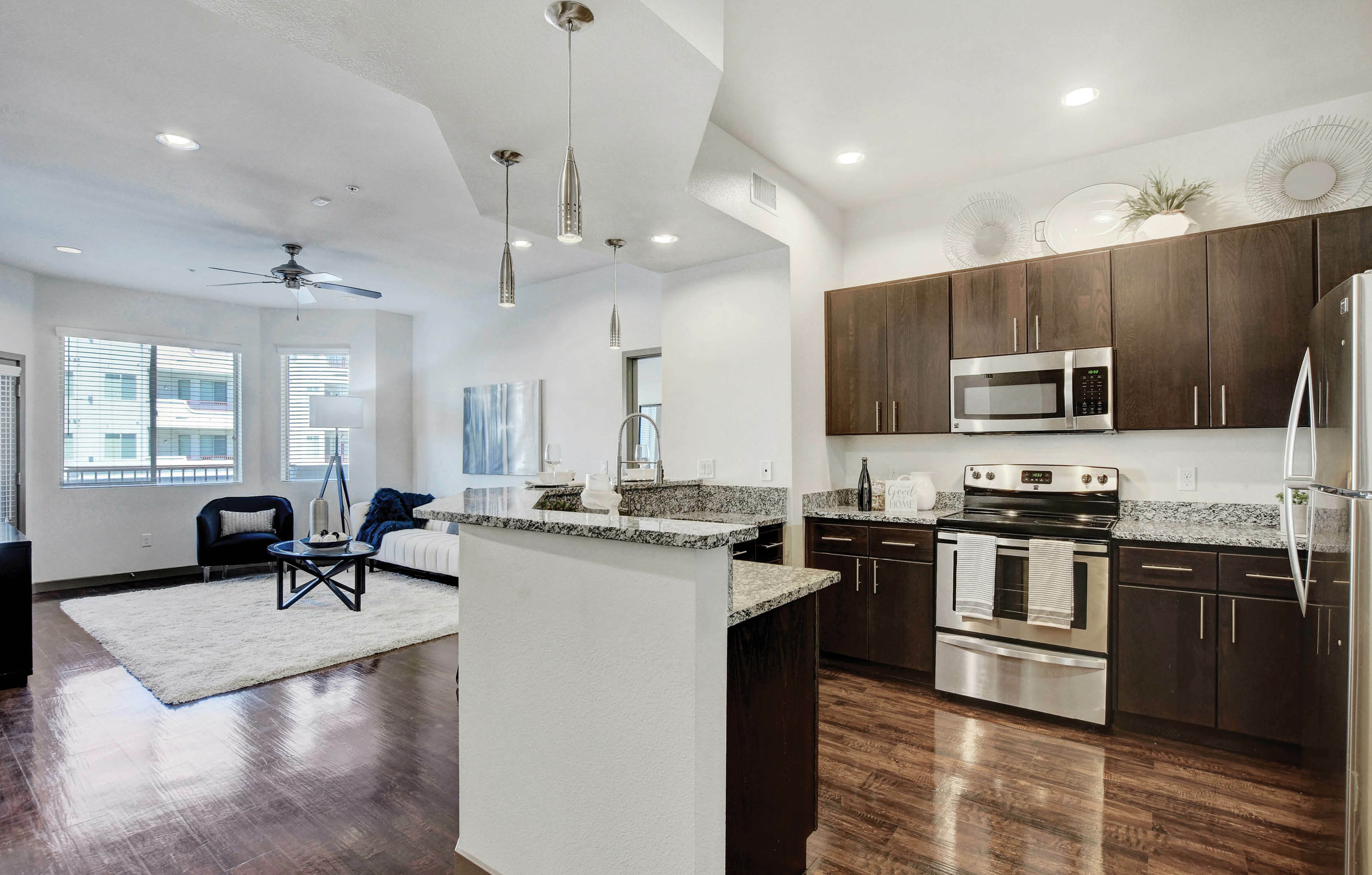 Modern open-concept kitchen and living room with granite countertops, dark wood cabinets, and stylish lighting fixtures.