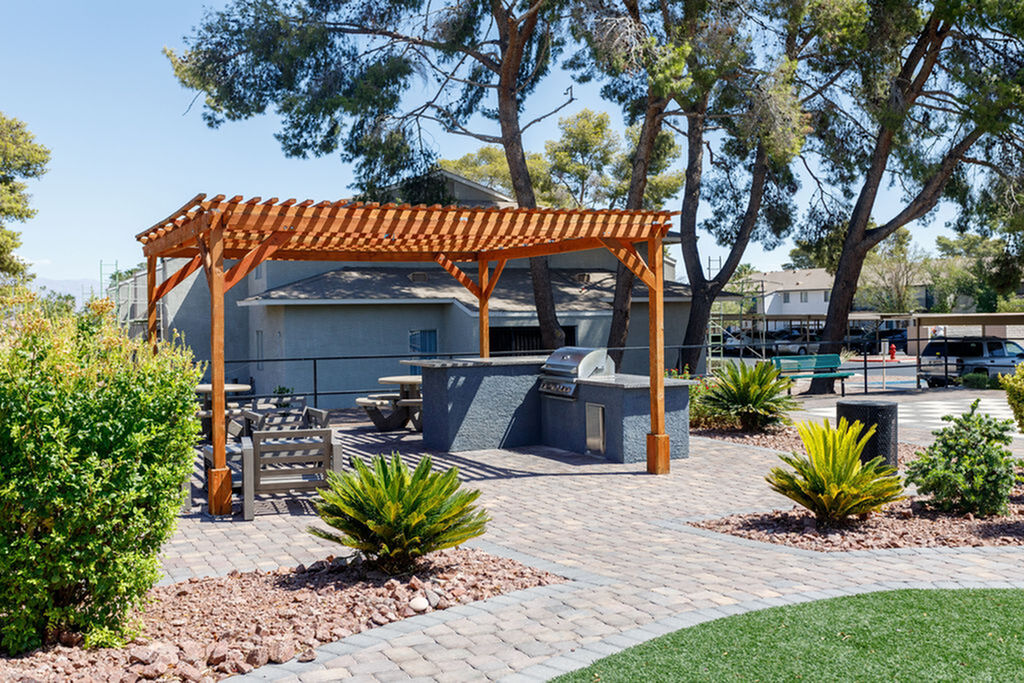 Inviting outdoor living space with a charming pergola, modern grill station, and lush greenery under tall trees, perfect for entertaining.