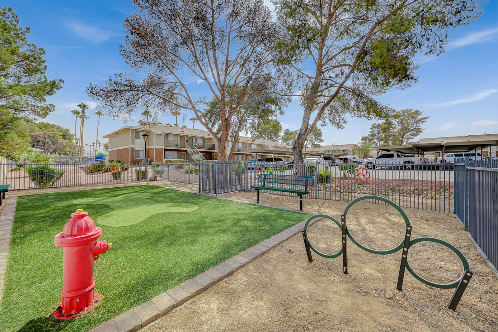 Inviting apartment complex courtyard featuring green lawns, a vibrant red fire hydrant, and playful circular bike racks under shady trees.