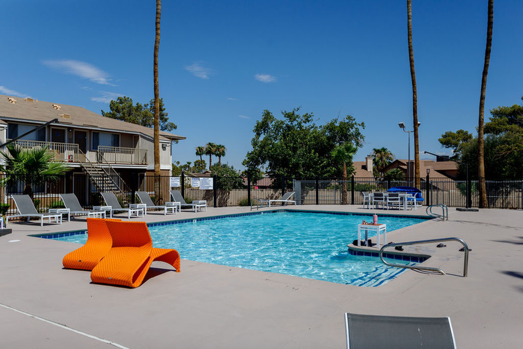 Inviting apartment complex pool area with modern lounge chairs, surrounded by lush palm trees and vibrant blue skies.