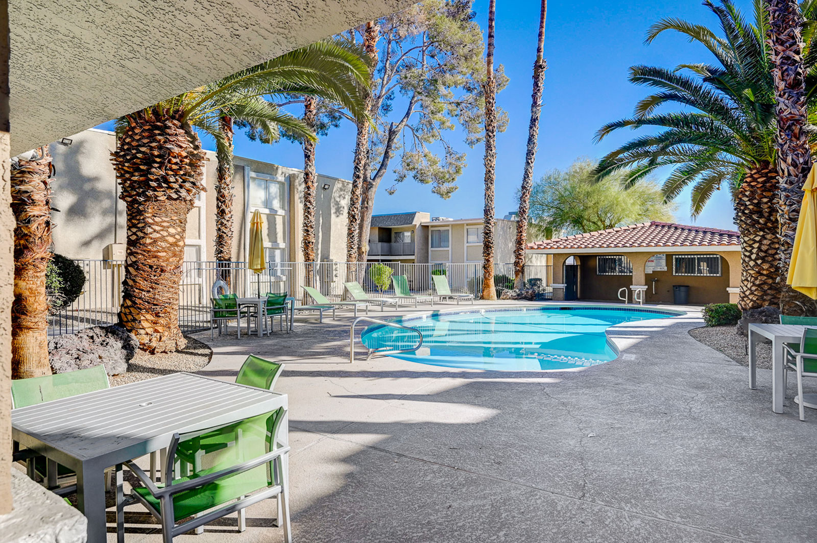 Charming apartment complex featuring a sunlit pool area surrounded by lush palm trees and inviting lounge chairs for relaxation.