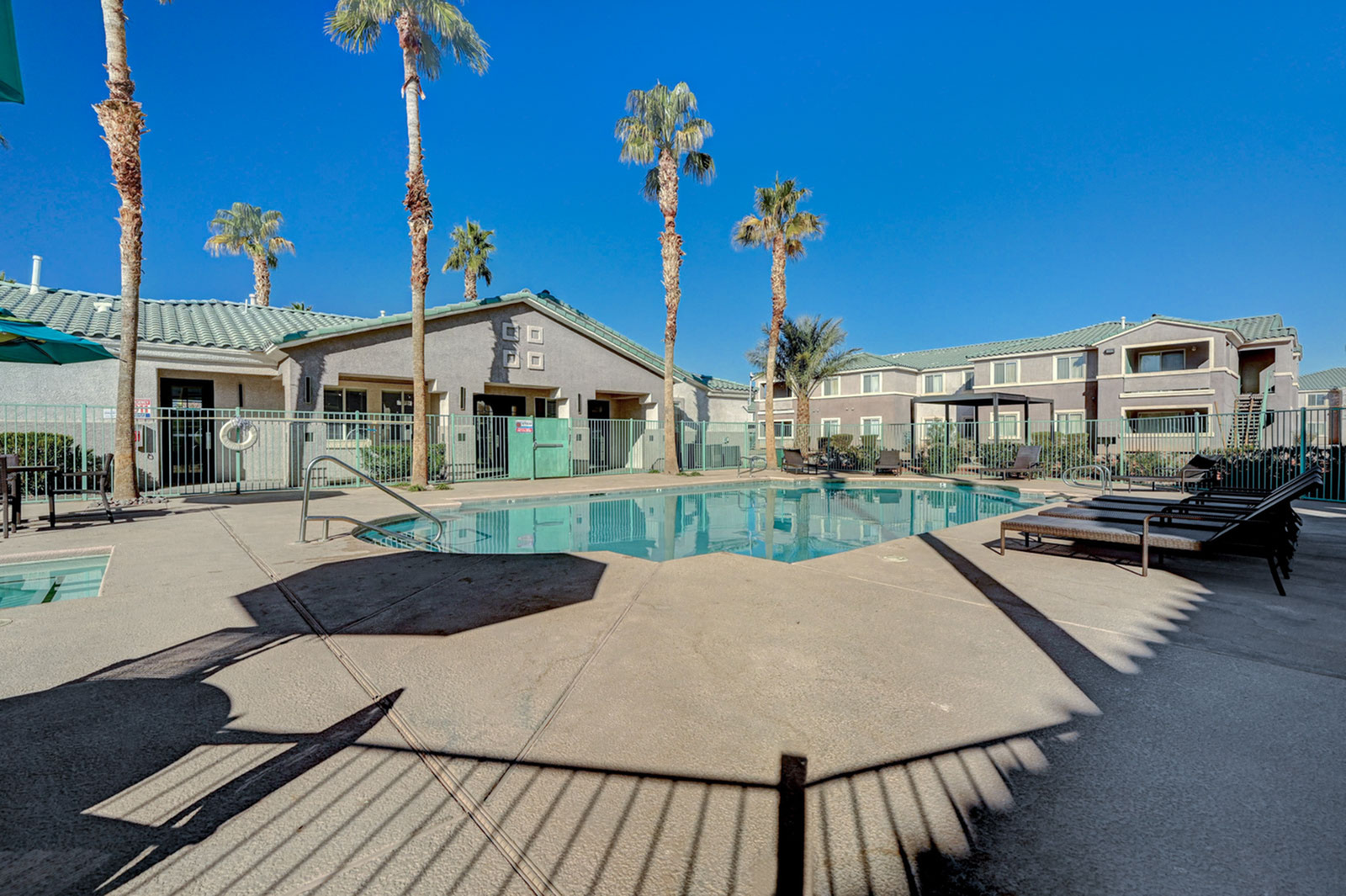 Inviting apartment complex featuring a sparkling pool surrounded by lounge chairs and palm trees, set against a clear blue sky.