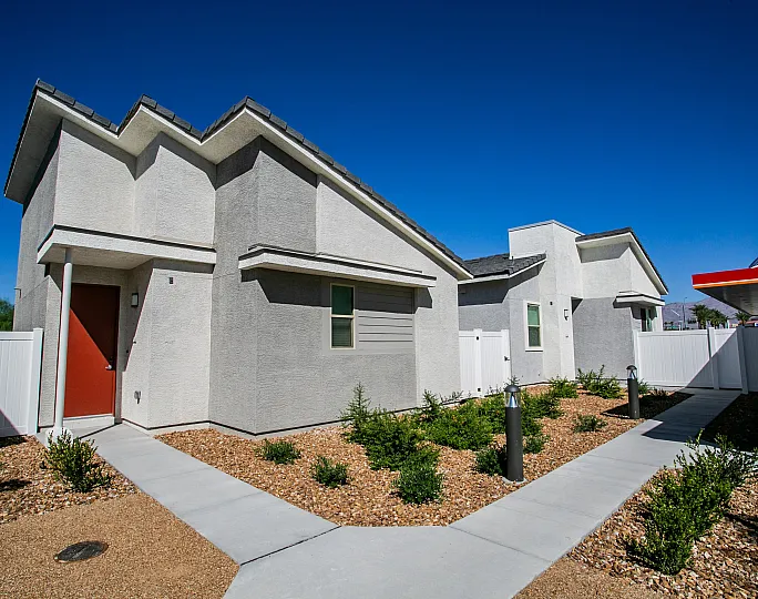 Contemporary desert home with white exterior, red door, and landscaped pathway under a clear blue sky.