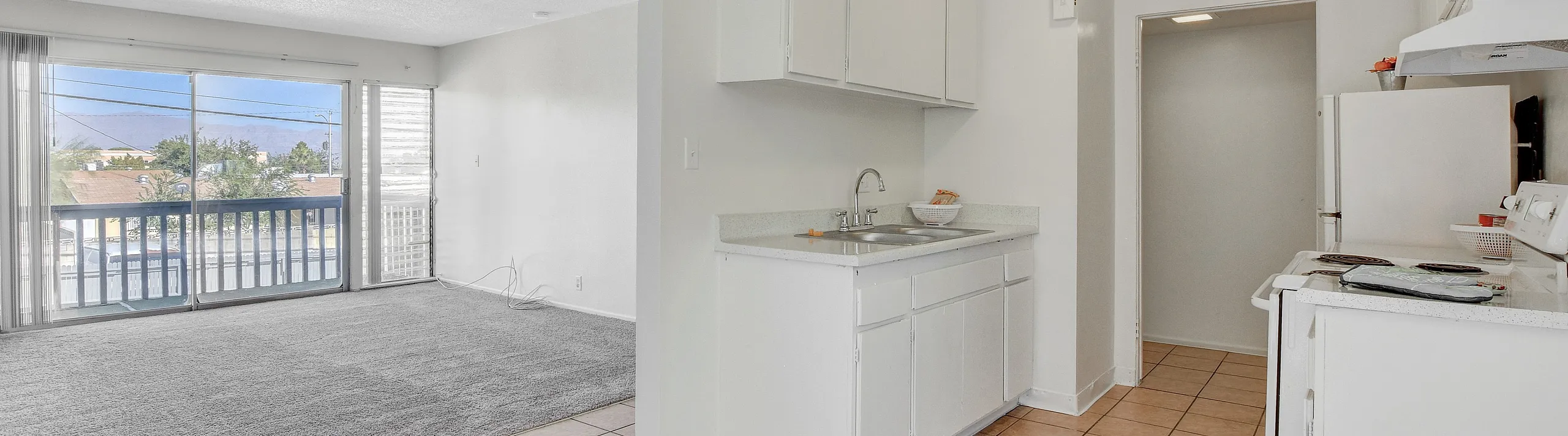 Inviting open-concept area with tiled kitchen and carpeted living room, featuring large windows and ample sunlight.