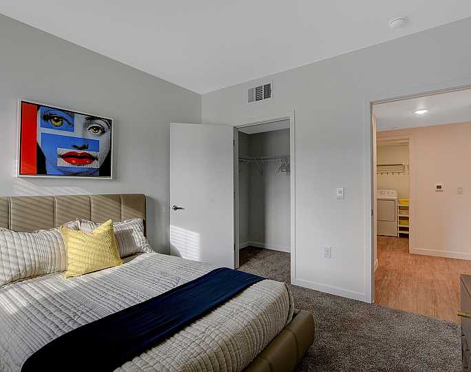 Inviting bedroom with modern decor, featuring a plush bed, vibrant artwork, and spacious closet access.