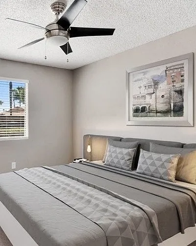 Bright bedroom with a stylish ceiling fan, comfortable bed, decorative wall art, and natural lighting from a window.