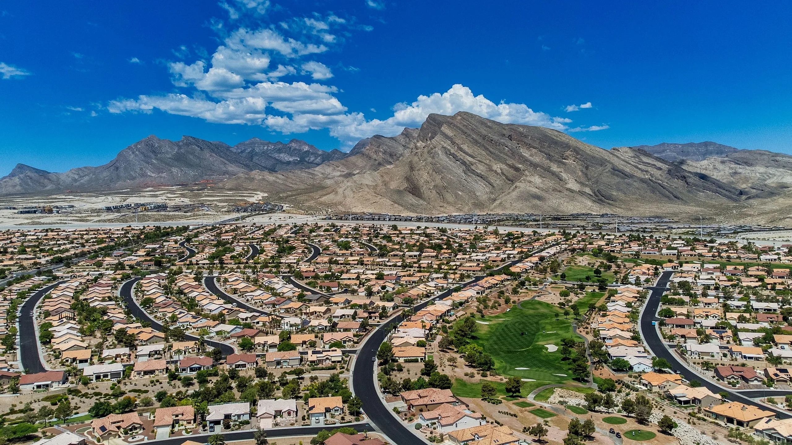 Breathtaking aerial view of a sunlit suburban neighborhood with winding roads and mountain backdrop.