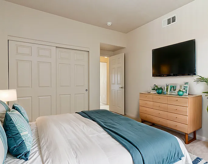 Charming bedroom featuring a stylish bed with blue accents, a sleek dresser, and a wall-mounted TV.