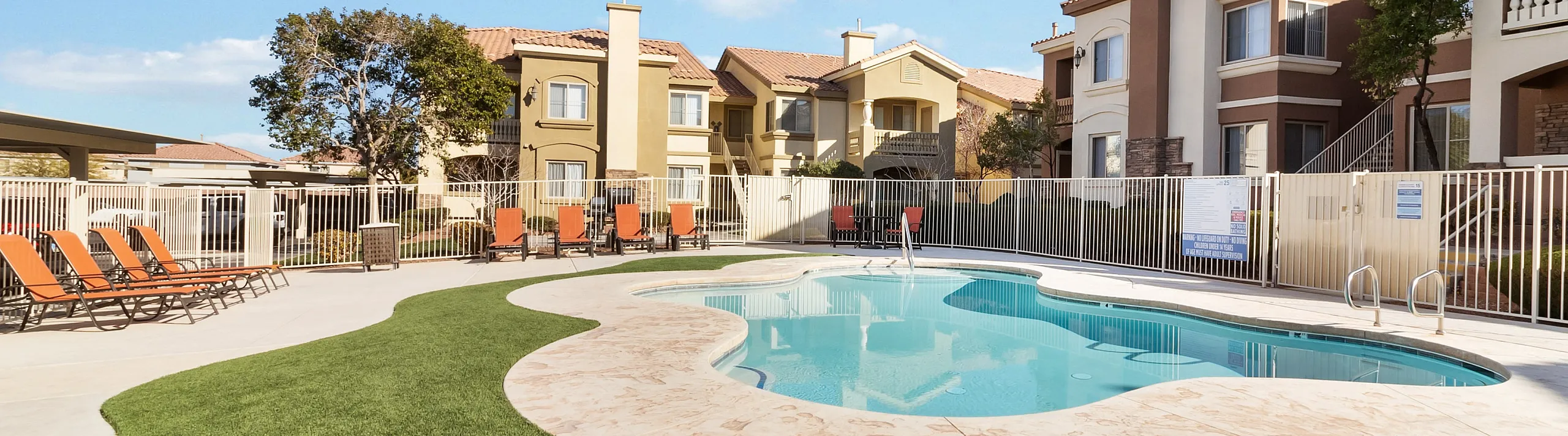 Modern apartment complex featuring a sunlit swimming pool surrounded by comfortable loungers and vibrant green landscape.