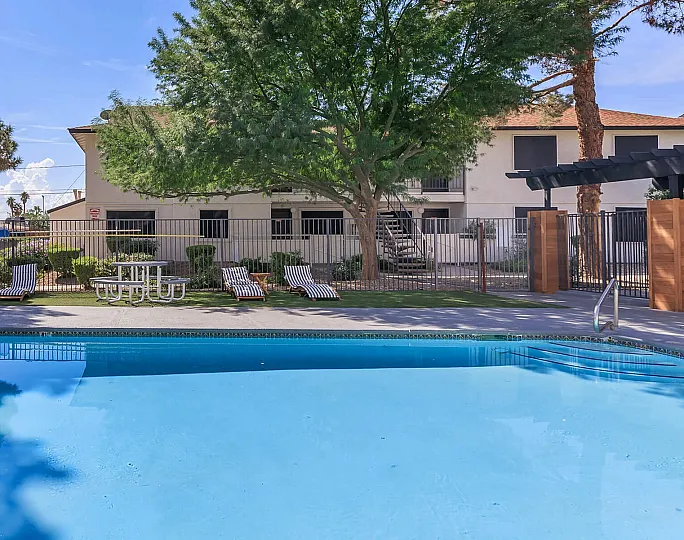 Inviting outdoor pool area with lounge chairs, lush greenery, and sunlit blue water.