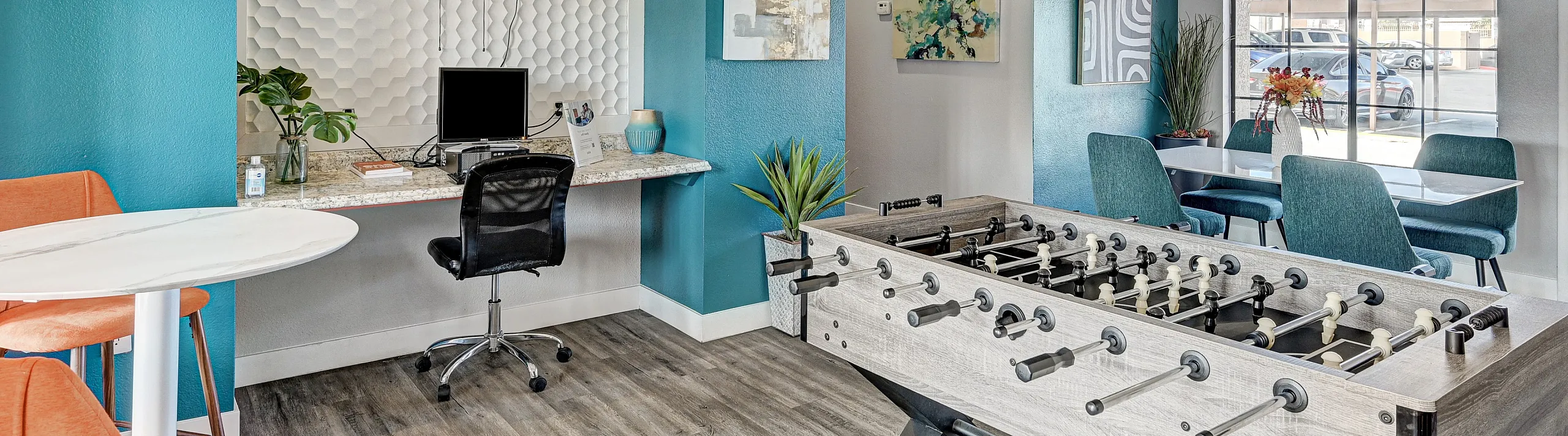 Modern apartment common area with vibrant teal accents, featuring a sleek foosball table, stylish seating, and contemporary wall art, perfect for socializing and relaxation.