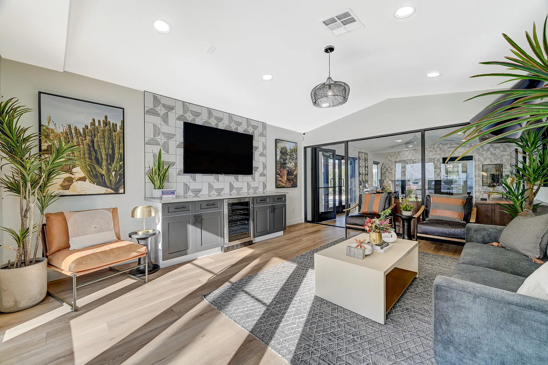 Modern living room with elegant decor, featuring cozy seating, a stylish coffee table, and vibrant greenery. Abundant natural light highlights a sleek media wall and contemporary design.