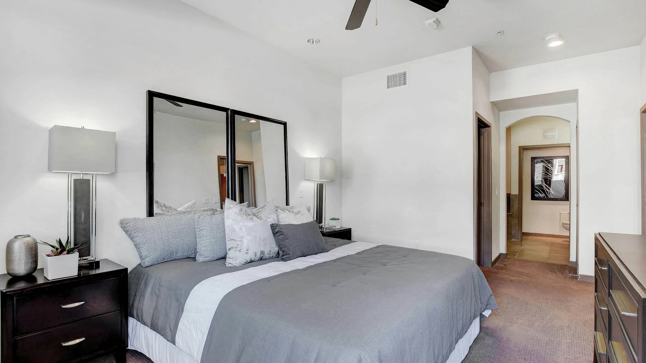 Elegant bedroom interior with a cozy king-sized bed, stylish lamps, and a modern ceiling fan, leading to a chic en-suite bathroom.