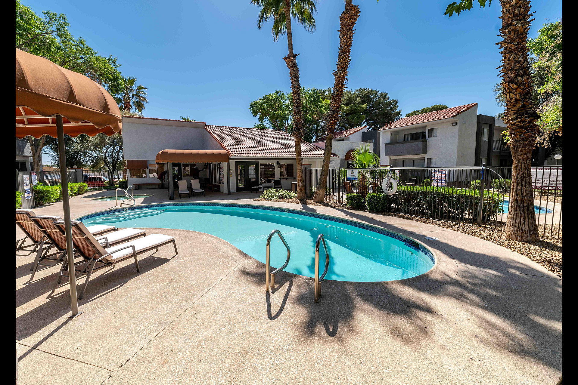 Inviting outdoor pool area with sun loungers, surrounded by scenic palm trees and modern residential buildings, ideal for relaxation.