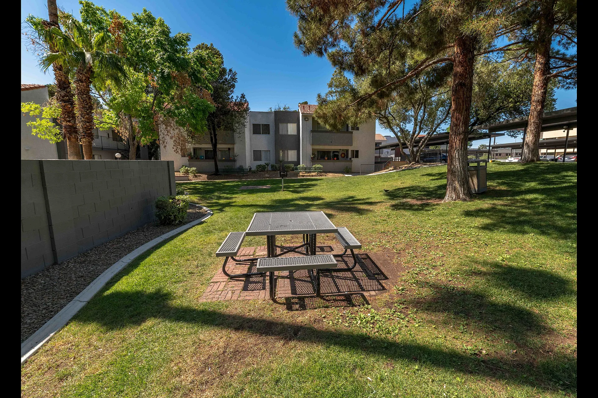 Tranquil apartment courtyard with lush green grass, picnic table, and surrounding trees, offering a peaceful outdoor retreat.