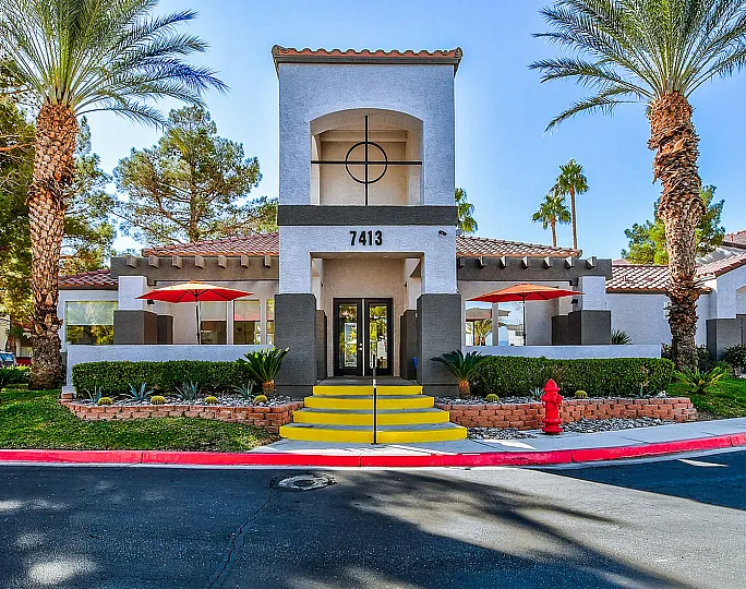 Inviting entrance of a modern apartment complex surrounded by lush palm trees and vibrant landscape on a sunny day.