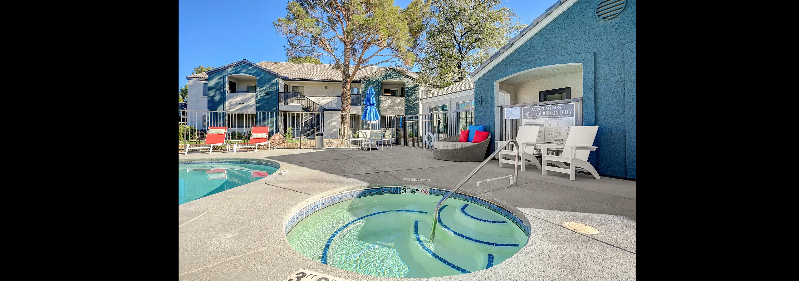Inviting outdoor area with a sparkling hot tub and pool, surrounded by stylish lounge seating, vibrant blue umbrellas, and charming apartment buildings in the background.
