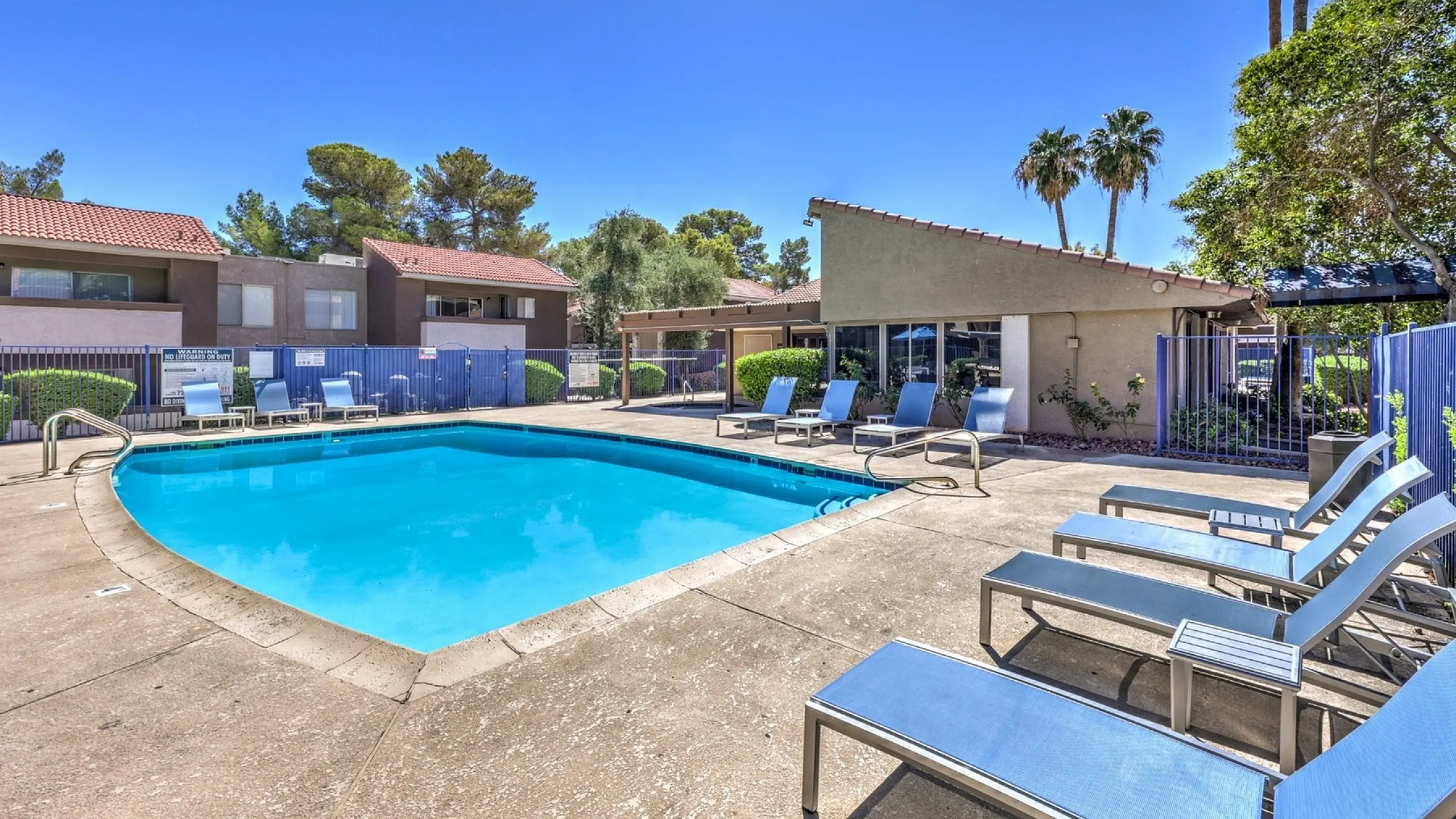 Inviting outdoor pool area surrounded by modern lounge chairs, elegant fencing, and lush greenery, perfect for relaxation and leisure.