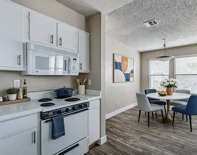 Modern kitchen and dining area featuring sleek white cabinets, contemporary appliances, and a cozy table with stylish blue and gray chairs.