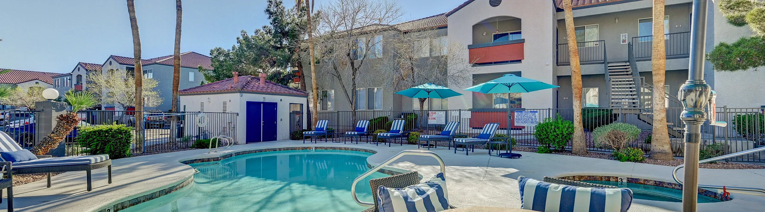 Inviting apartment pool area with palm trees, plush loungers, and vibrant umbrellas, offering a serene oasis for relaxation.