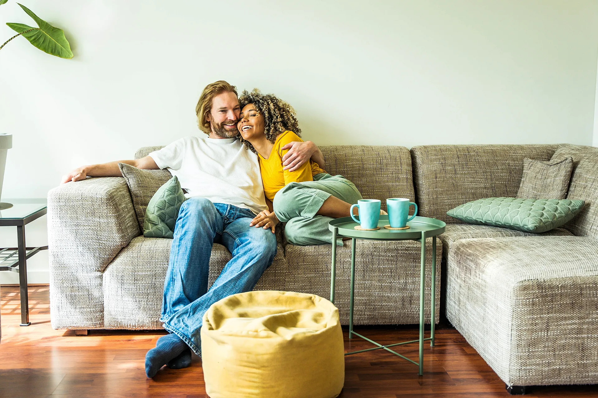 Inviting living room with a cozy L-shaped sofa, vibrant pillows, and a couple enjoying their peaceful morning with coffee mugs on a stylish side table.
