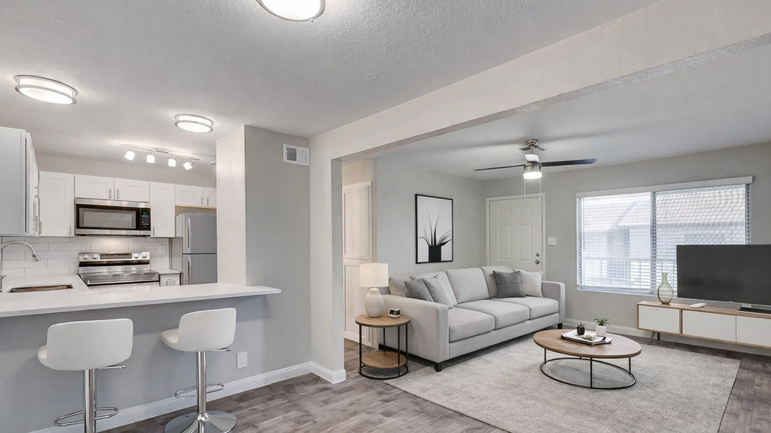 Modern open-plan living room with sleek kitchen, featuring stylish bar seating, cozy gray sofa, and bright natural lighting.