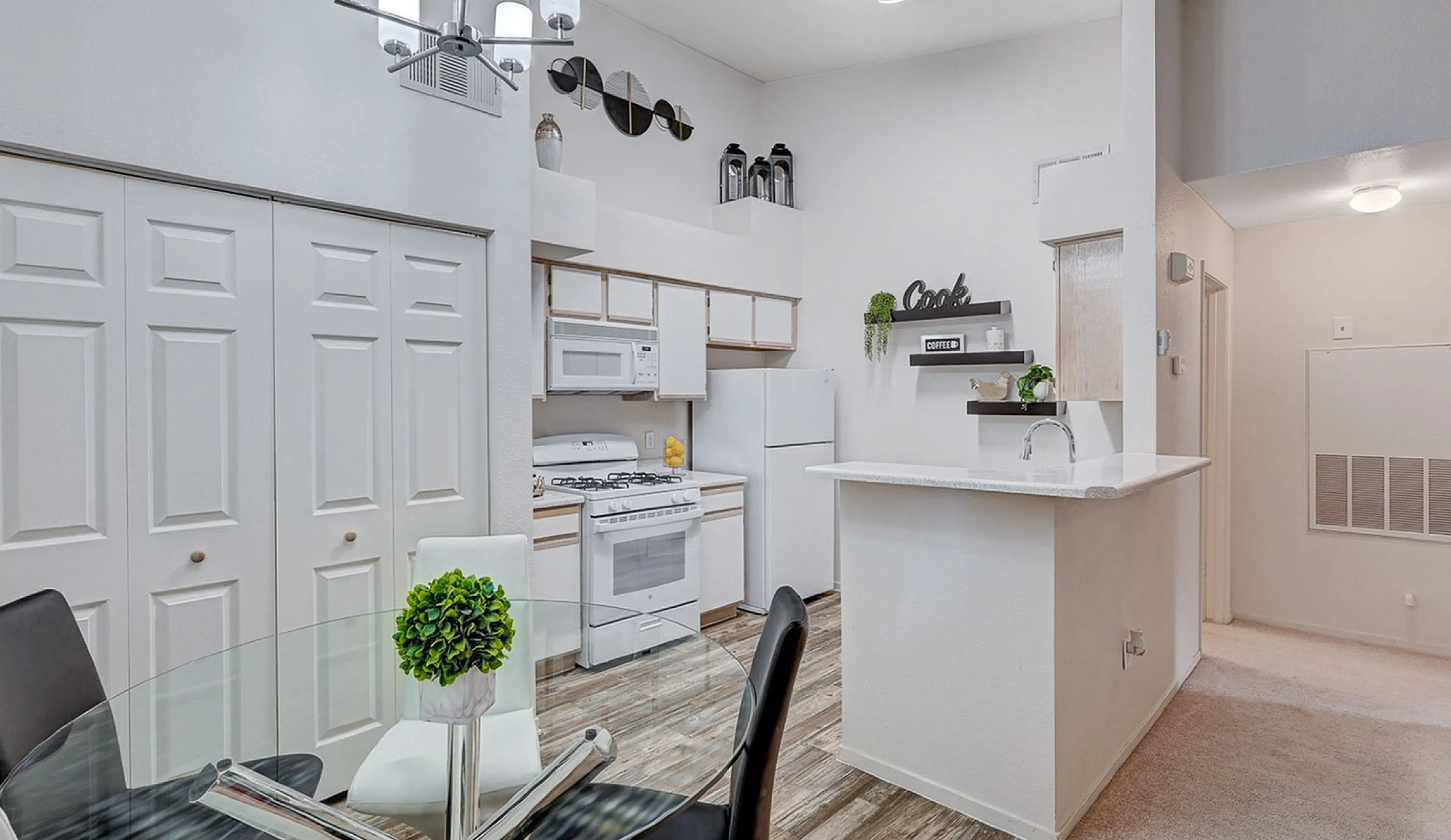 Modern kitchen with open layout and stylish dining area, featuring sleek white cabinets, contemporary lighting, and elegant decor.
