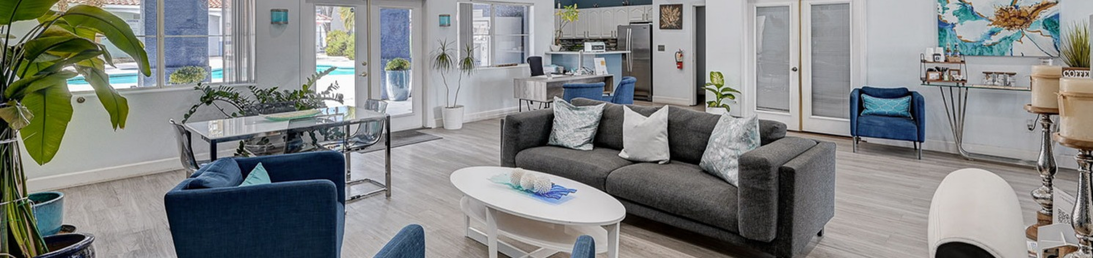 Modern open-concept living space with stylish decor, plush gray sofa, vibrant blue chairs, and natural light streaming in through large windows, offering a bright and inviting atmosphere.