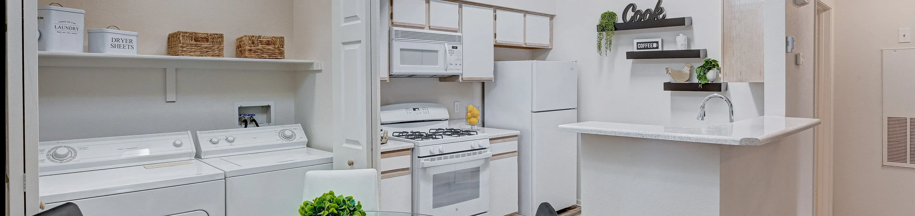 Elegant apartment kitchen with sleek white cabinets, a gas range, and cozy dining area adjacent to a convenient in-unit laundry space, complemented by a stylish chandelier and modern decor.