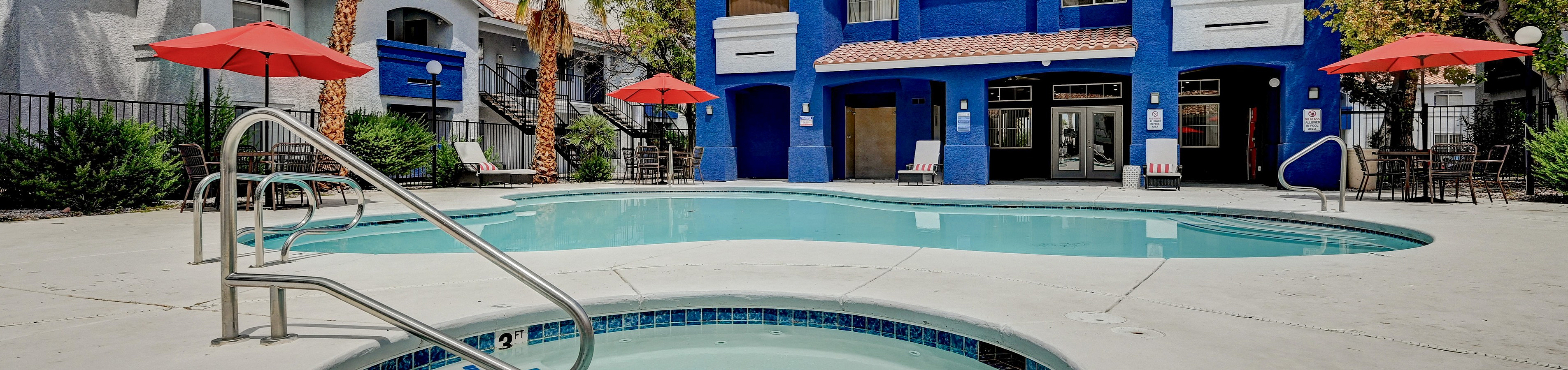 Vibrant apartment exterior with a sparkling pool and jacuzzi, surrounded by lush palm trees and red umbrellas, perfect for relaxation and leisure.