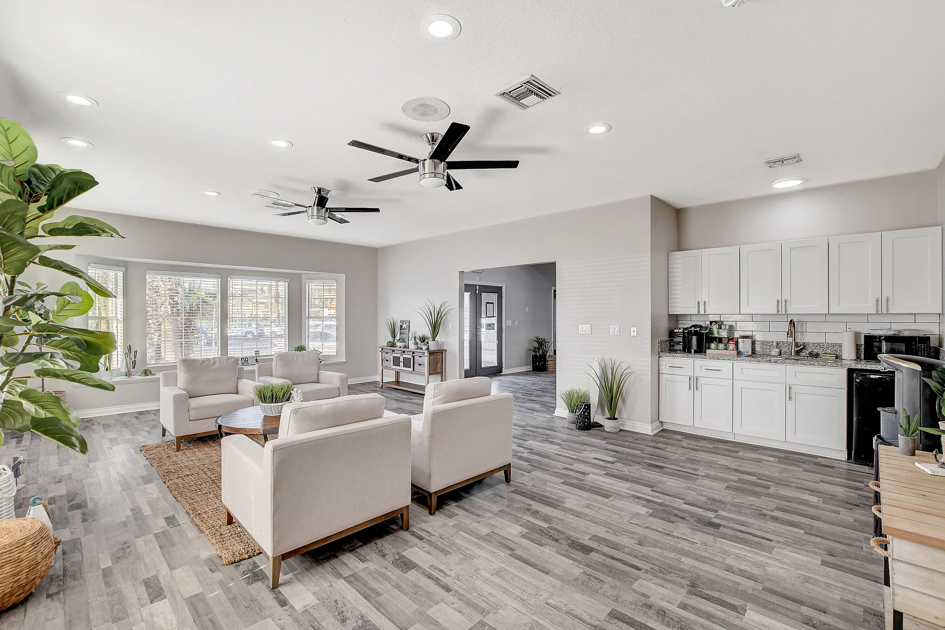 Bright and modern open-concept living space featuring sleek hardwood flooring, elegant white kitchen cabinets, and stylish ceiling fans, creating a welcoming and functional environment.