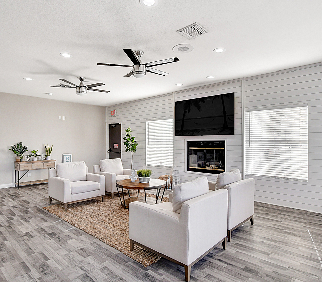 Bright and modern living area with plush white seating, stylish ceiling fans, and a large flat-screen TV, offering a welcoming and contemporary atmosphere.