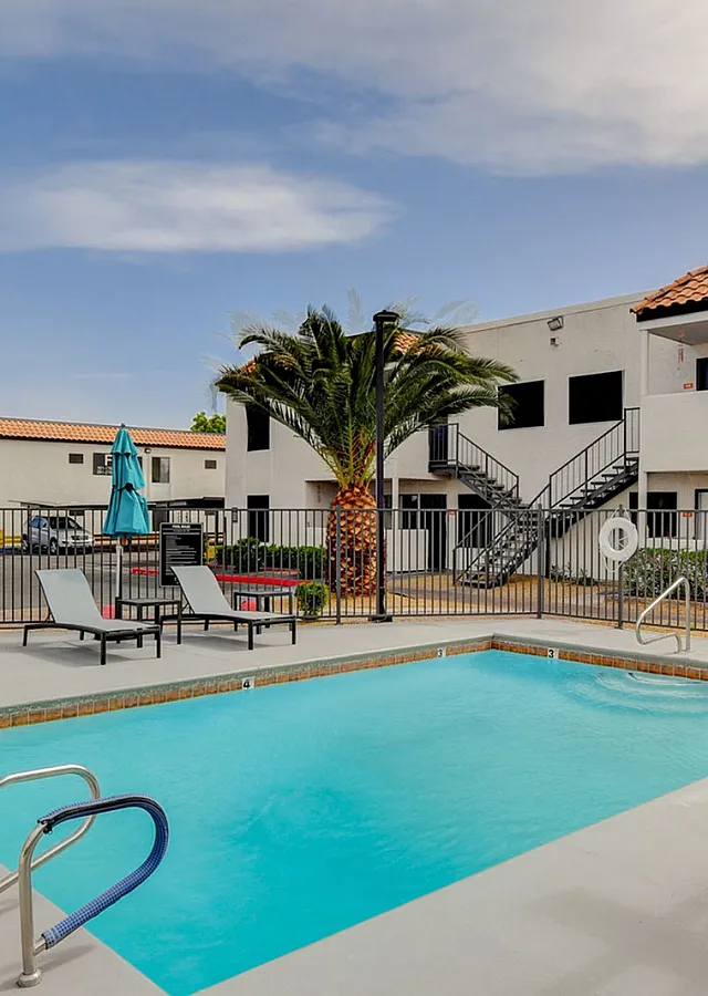 Charming apartment complex with a refreshing pool, sun loungers, and inviting outdoor space featuring palm trees.