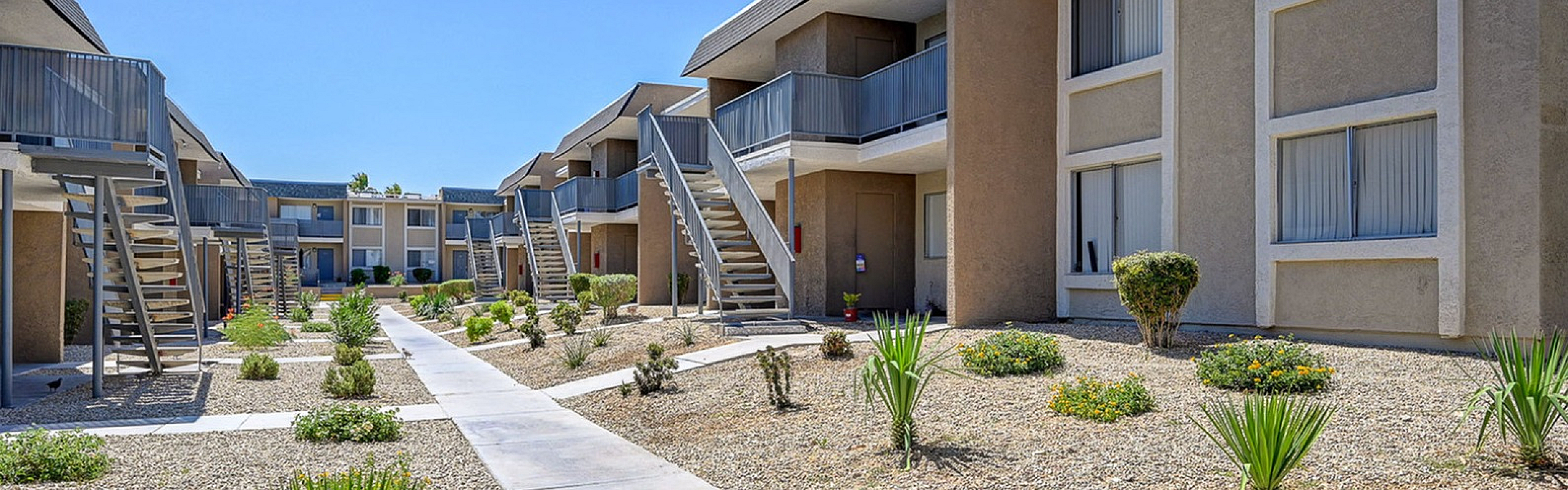 Modern apartment complex featuring stylish exterior with open staircases, elegant landscaping, and a sunlit courtyard.